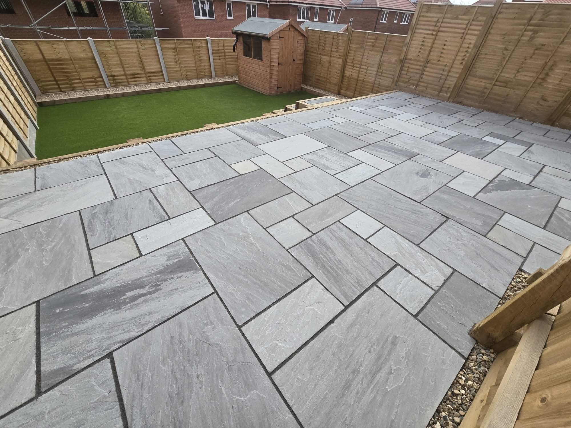 Grey porcelain patio with raised retaining wall and pebble infill beside lawn