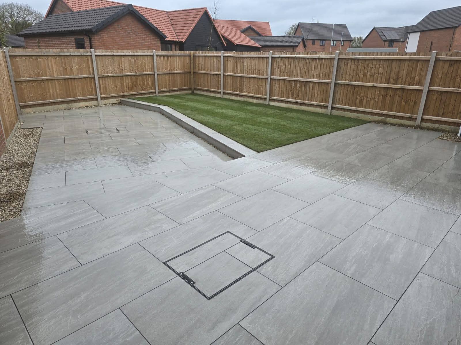 Large grey porcelain patio with raised lawn area and timber fencing