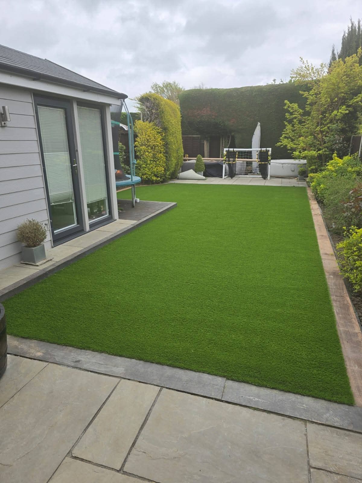 Artificial lawn with sandstone patio edging beside garden studio