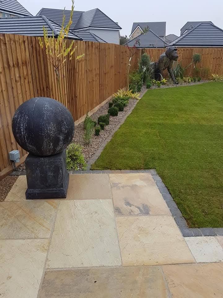 Sandstone patio with lawn, planted borders and stone sphere ornament