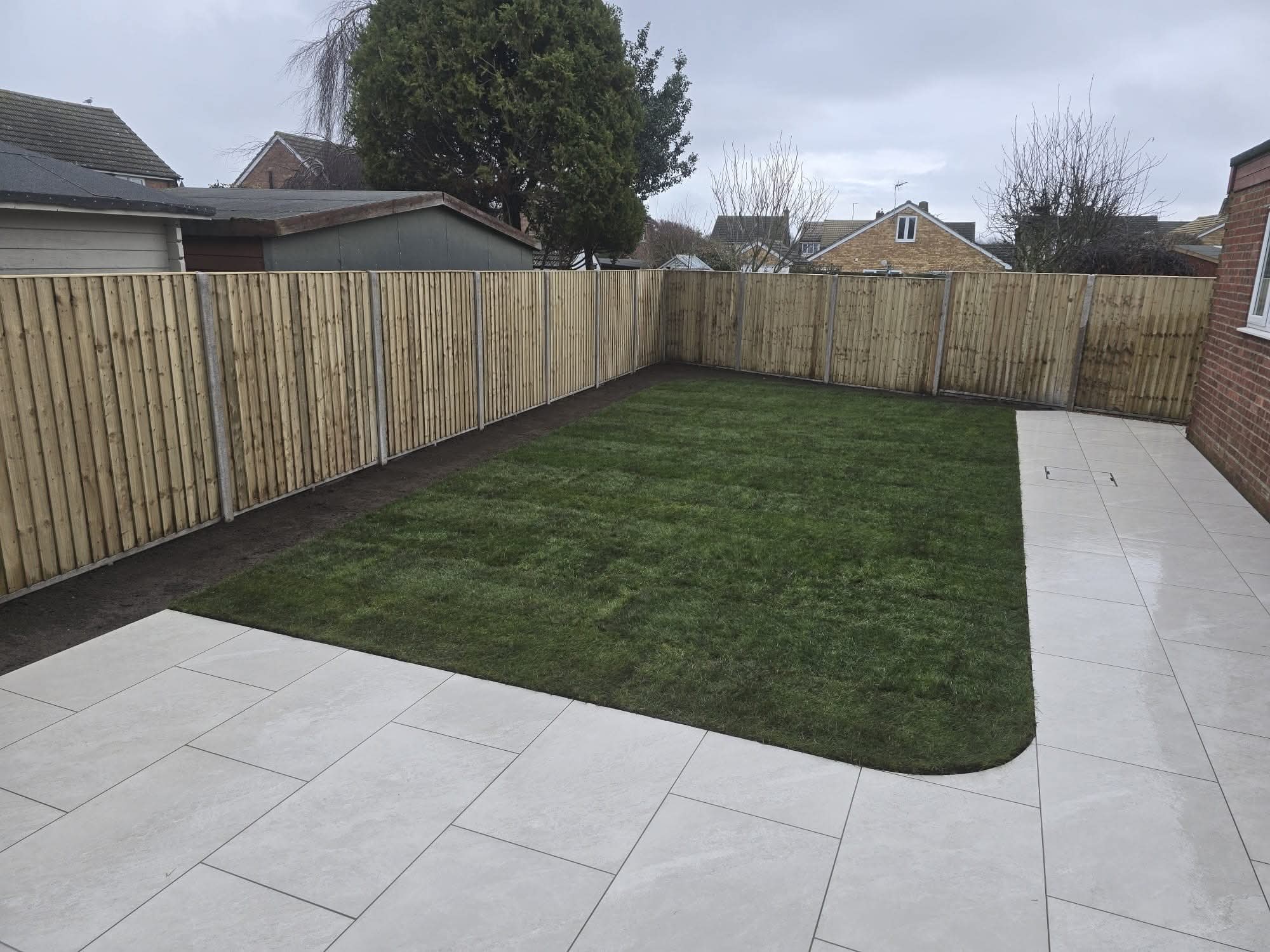 Grey porcelain patio with raised step and pebble drainage channel beside lawn